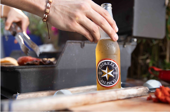Una persona sosteniendo una botella de cerveza Estrella Jalisco.