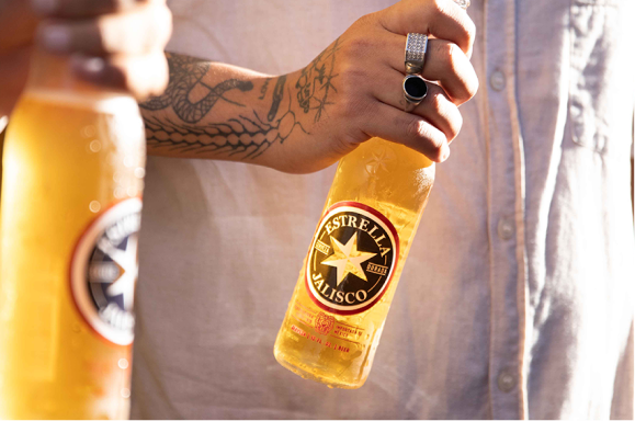 Persona sosteniendo una botella de Estrella Jalisco.